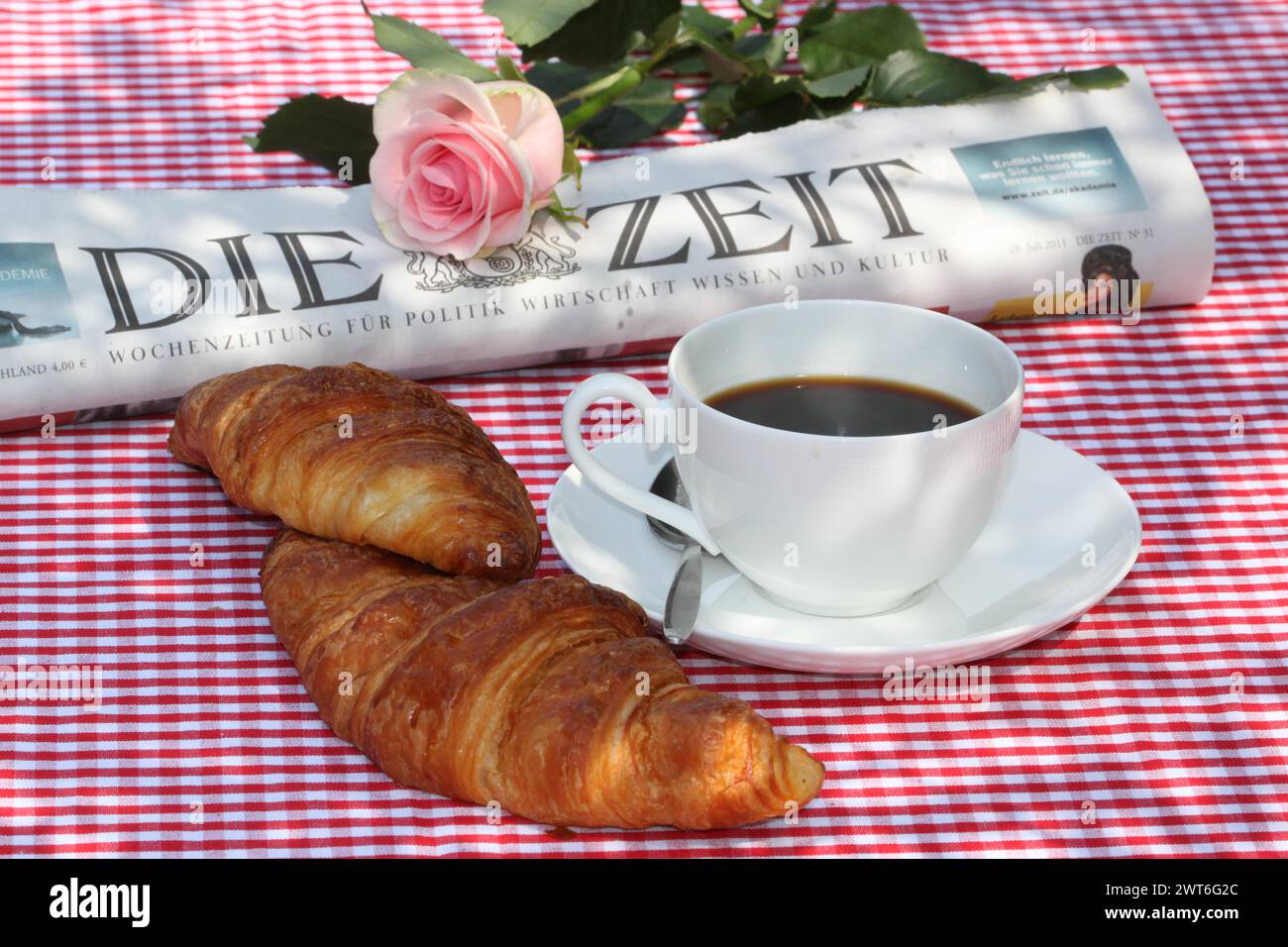 Ein traditionelles Fruehstueck mit Kaffee und croissants auf einer rot-karierten Tischdecke mit Zeitung und Rose im Hintergrund, Deutschland Banque D'Images