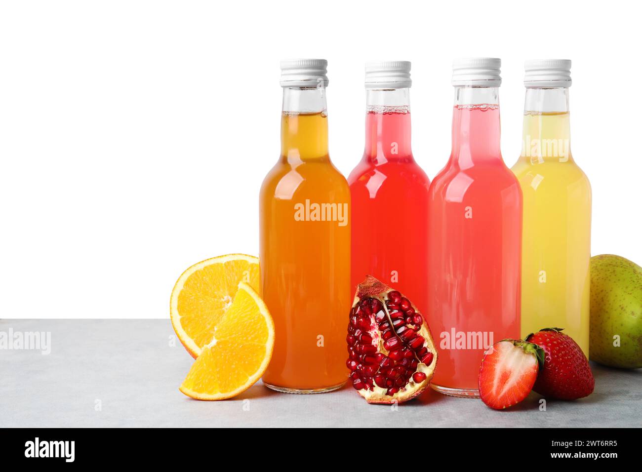 Délicieux kombucha dans des bouteilles en verre et des fruits frais sur une table grise sur fond blanc Banque D'Images