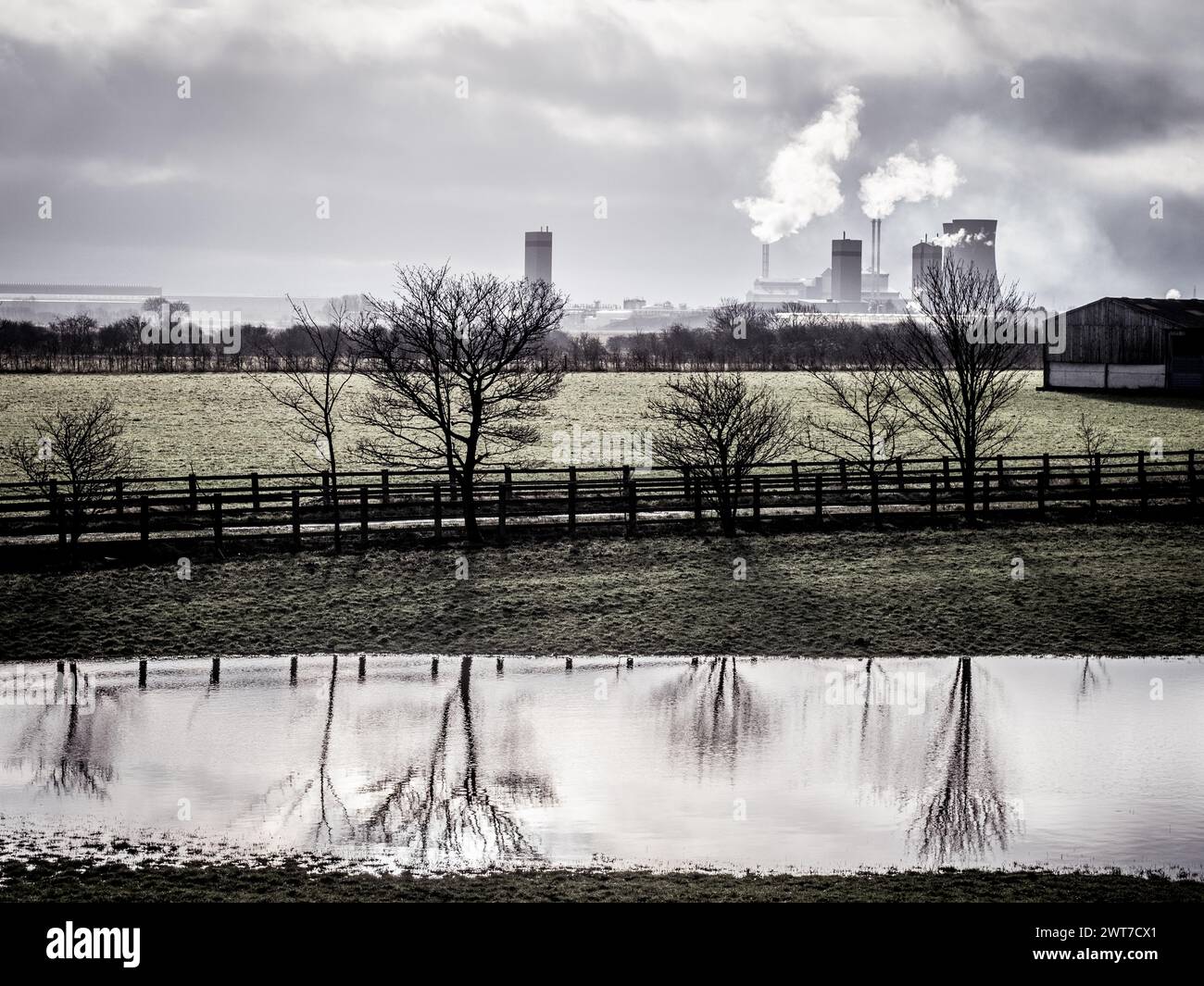 Les arbres se reflètent dans un champ creusé d'eau, les centrales électriques peuvent être vues au loin vers la ville industrielle de Middlesbrough dans le nord-est. ROYAUME-UNI. Banque D'Images