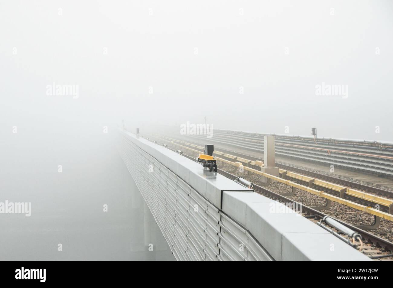 Ligne de métro surélevée se dégageant dans le brouillard. Rails sur un pont au-dessus d'une rivière - faible visibilité. Trajet matinal - attente d'un train. Vue en perspective Banque D'Images