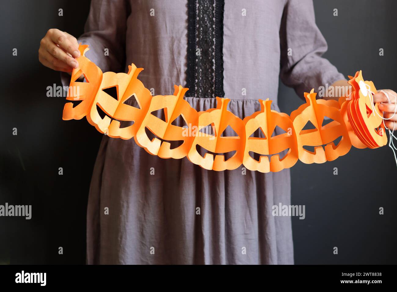 Femme en robe gothique grise tient une guirlande de papier. Guirlande de citrouille sur fond sombre. Décorations d'Halloween écologiques faites à la main. Banque D'Images