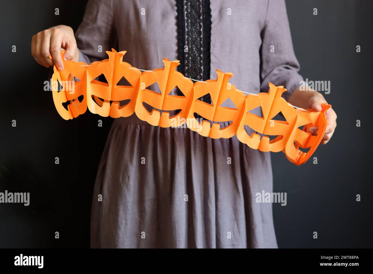 Femme en robe gothique grise tient une guirlande de papier. Guirlande de citrouille sur fond sombre. Décorations d'Halloween écologiques faites à la main. Banque D'Images