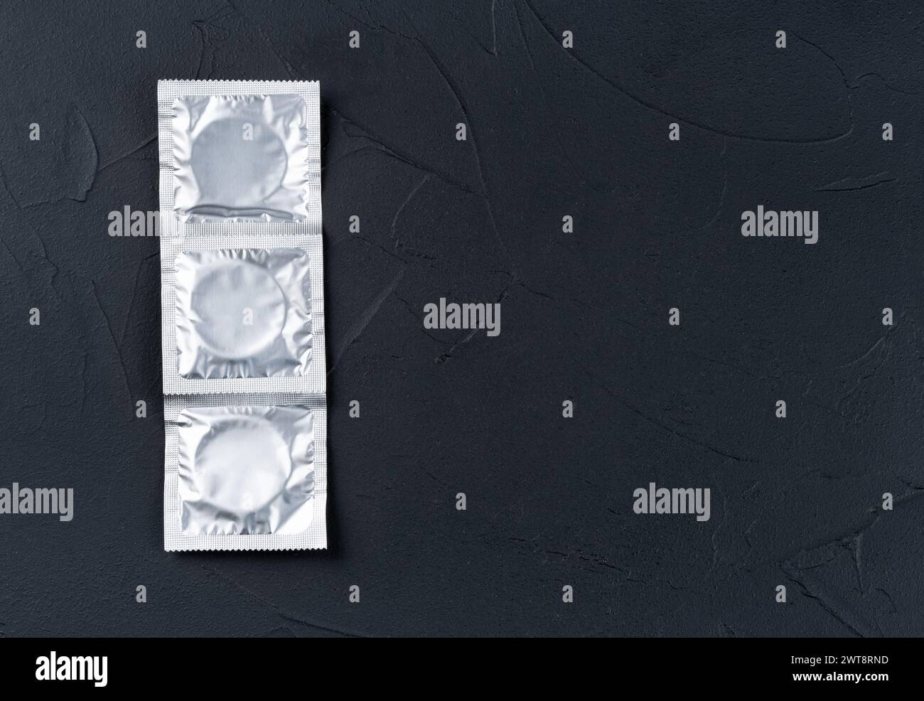 Trois préservatifs dans un emballage sur un fond sombre vide, vue de dessus. Copier l'espace Banque D'Images