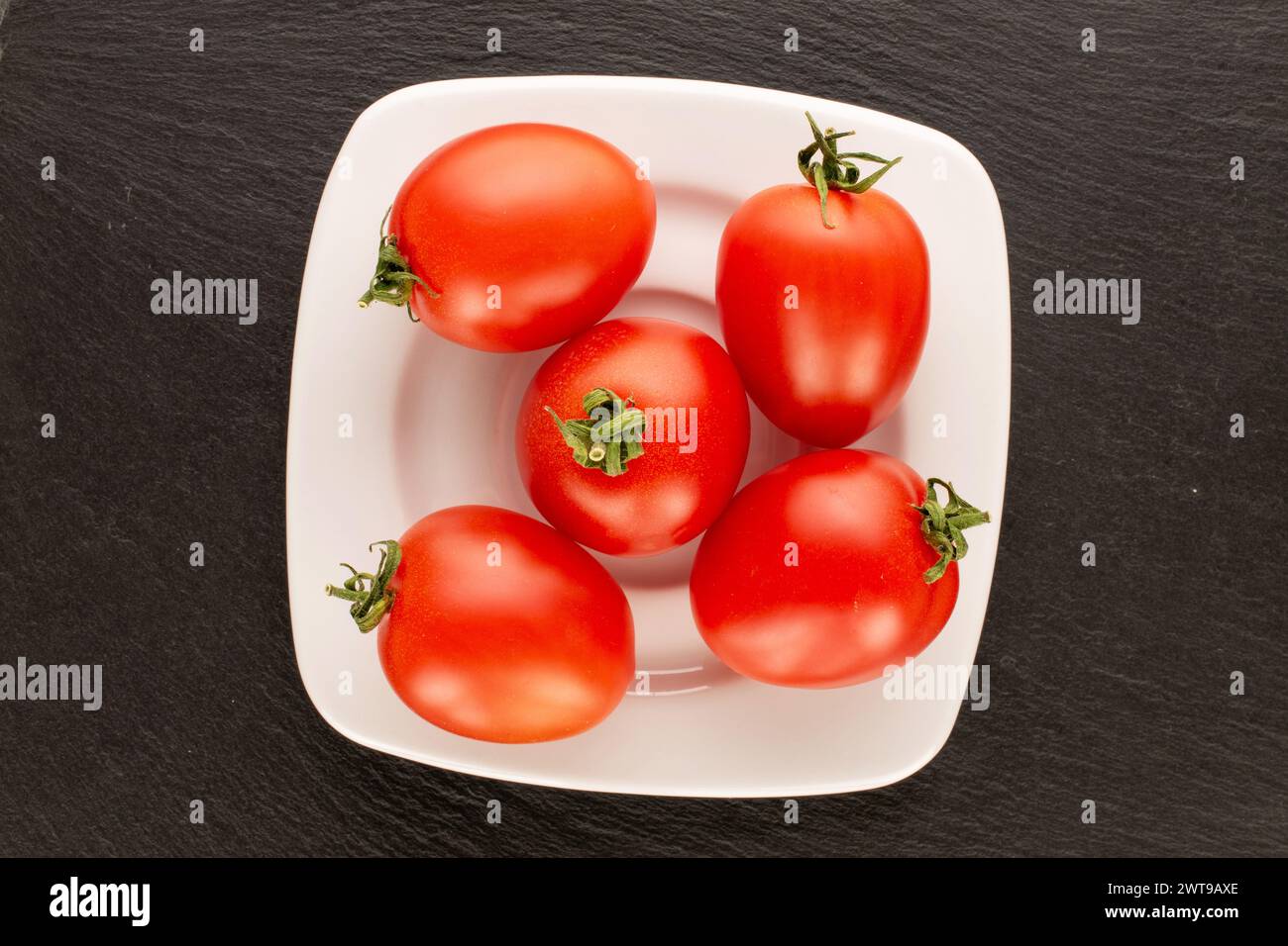 Plusieurs tomates cocktail avec plaque en céramique blanche sur pierre d'ardoise, macro, vue de dessus. Banque D'Images