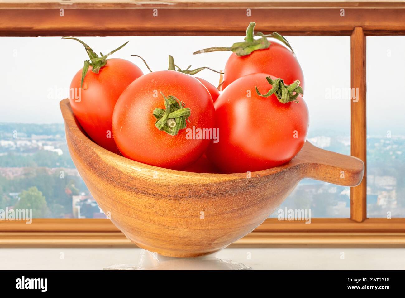 Quelques tomates cerises mûres dans une tasse en bois sur une table près de la fenêtre, macro. Banque D'Images