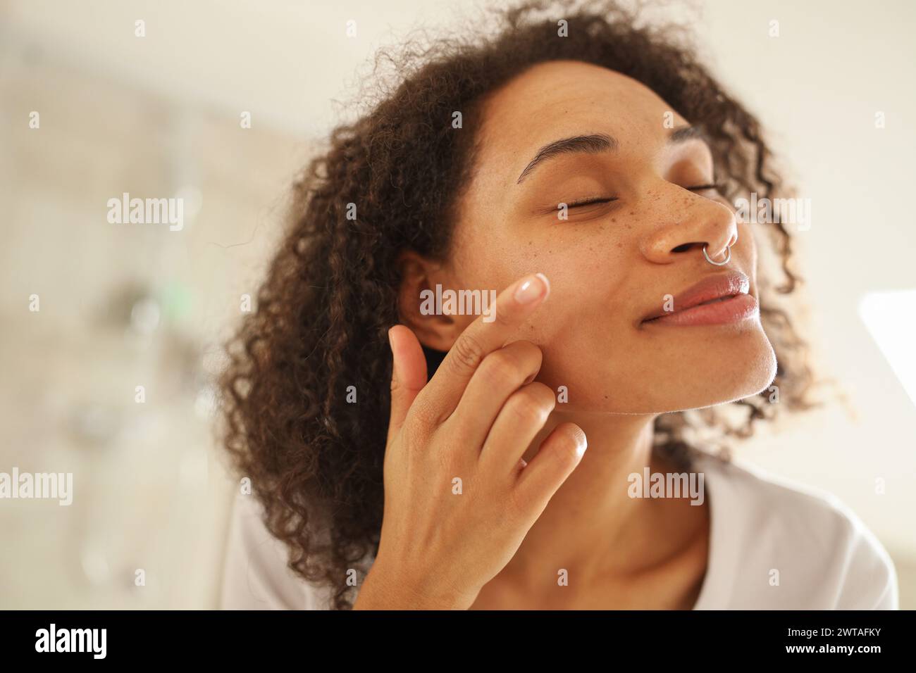 Femme appliquant la lotion sur son front, joue et cou devant le miroir Banque D'Images