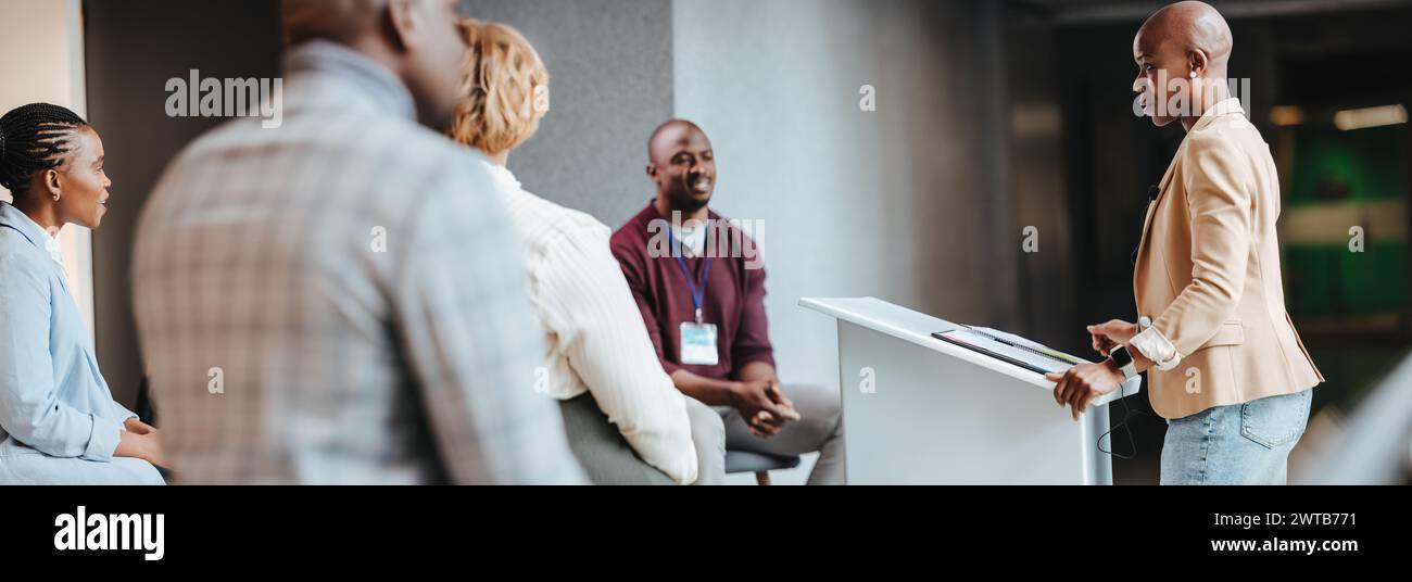 Femme d'affaires concentrée présentant à des collègues engagés lors d'une réunion d'équipe dans un environnement de bureau contemporain. L'image capture un trai d'entreprise Banque D'Images