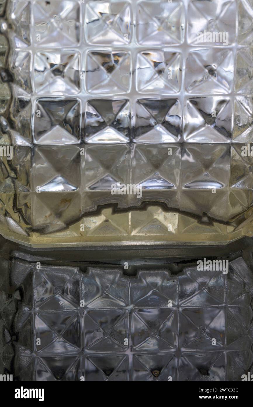 Détail d'hexagones carrés pointus de bouteille de liqueur en verre sculpté illuminés verticalement par réflexion Banque D'Images