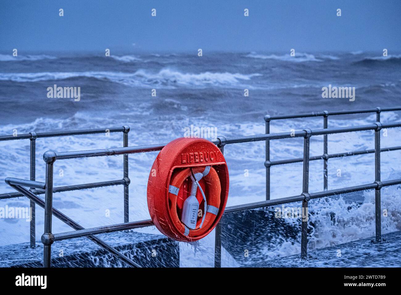 Bouée de sauvetage sur les rampes au bord de mer de Tiegnmouth lors d'une tempête avec une mer agitée. Banque D'Images