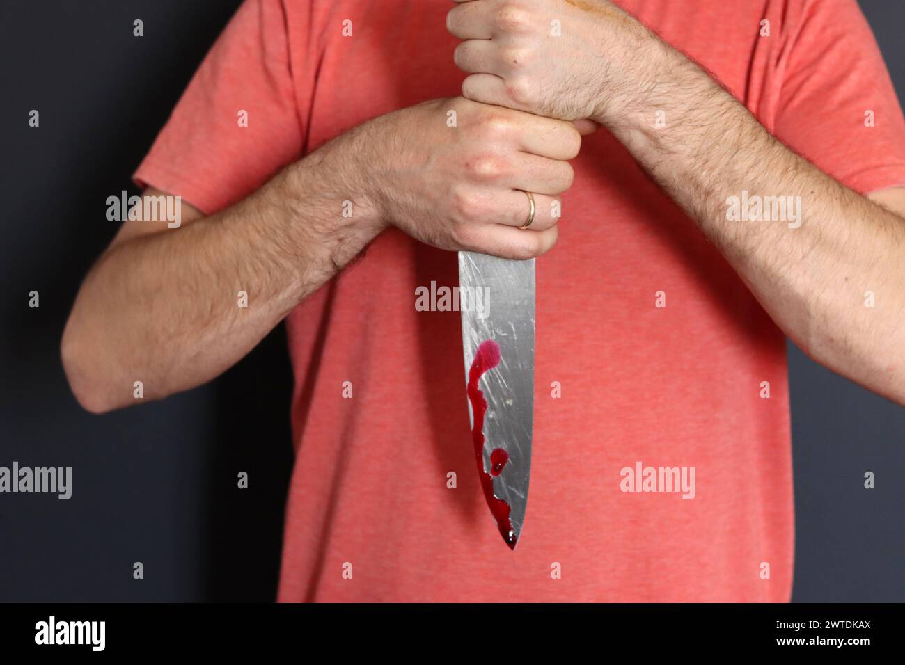 Homme tenant couteau avec du sang sur fond sombre, gros plan. Concept de violence domestique Banque D'Images