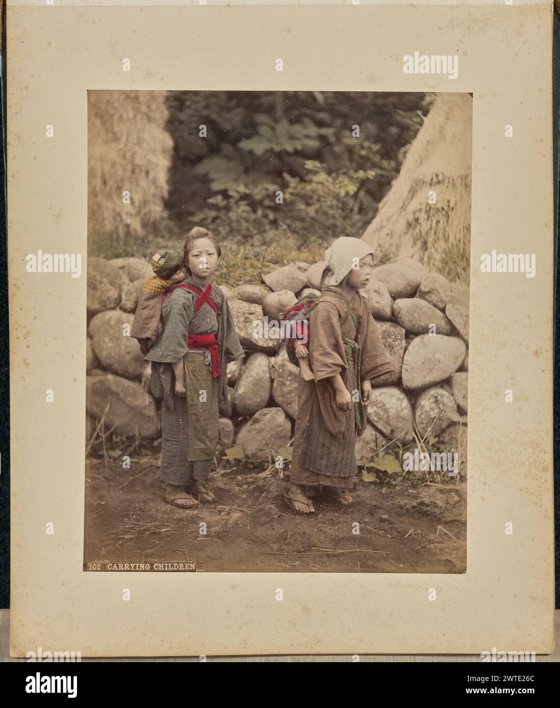 Porter des enfants. Attribué à Adolfo Farsari, photographe (américain, 1841 - 1898) des années 1875 à 1890, deux filles portent chacune un bébé endormi sur le dos. Une des filles a les cheveux couverts. (Recto, impression) en bas à gauche, imprimé en négatif : « 102 PORTANT DES ENFANTS »; Banque D'Images