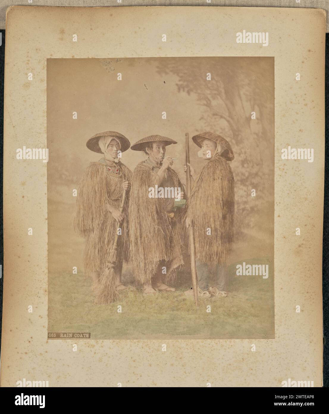 Imperméables. Attribué à Adolfo Farsari, photographe (américain, 1841 - 1898) des années 1875 à 1890 Portrait de studio de trois hommes portant des « mino », des imperméables japonais traditionnels fabriqués à partir de pailles. L'homme à gauche de l'image tient un balai de paille. (Recto, impression) en bas à gauche, imprimé en négatif : « 165 RAIN COAT »; Banque D'Images
