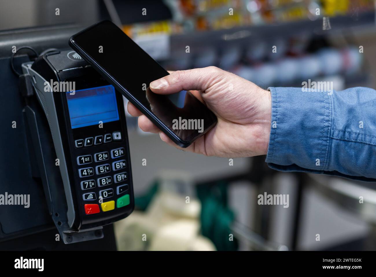 Gros plan d'une main masculine tenant un smartphone à un lecteur de carte pour le paiement mobile dans un magasin de détail. Banque D'Images