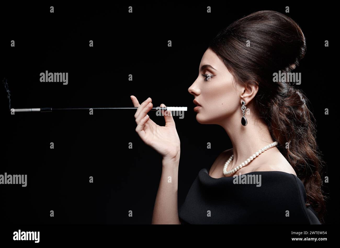 Plan rétro : la belle jeune femme fumant la cigarette. Portrait vintage de jolie fille dans le style des années 60. Magnifique dame en robe noire et collier de perles Banque D'Images