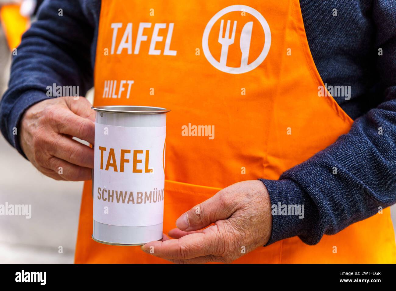 Schwabmünchen, Bavière, Allemagne - 17 mars 2024 : la banque alimentaire Schwabmünchen recueille des dons avec une canette lors du festival du printemps. Assistant bénévole avec un tablier orange avec le slogan, Tafel Hilft *** Die Tafel Schwabmünchen sammelt auf dem Frühlingsfest Geldspenden mit einer dose. Ehrenamtlicher Helfer mit einer orangen Schürze mit dem slogan, Tafel Hilft Banque D'Images