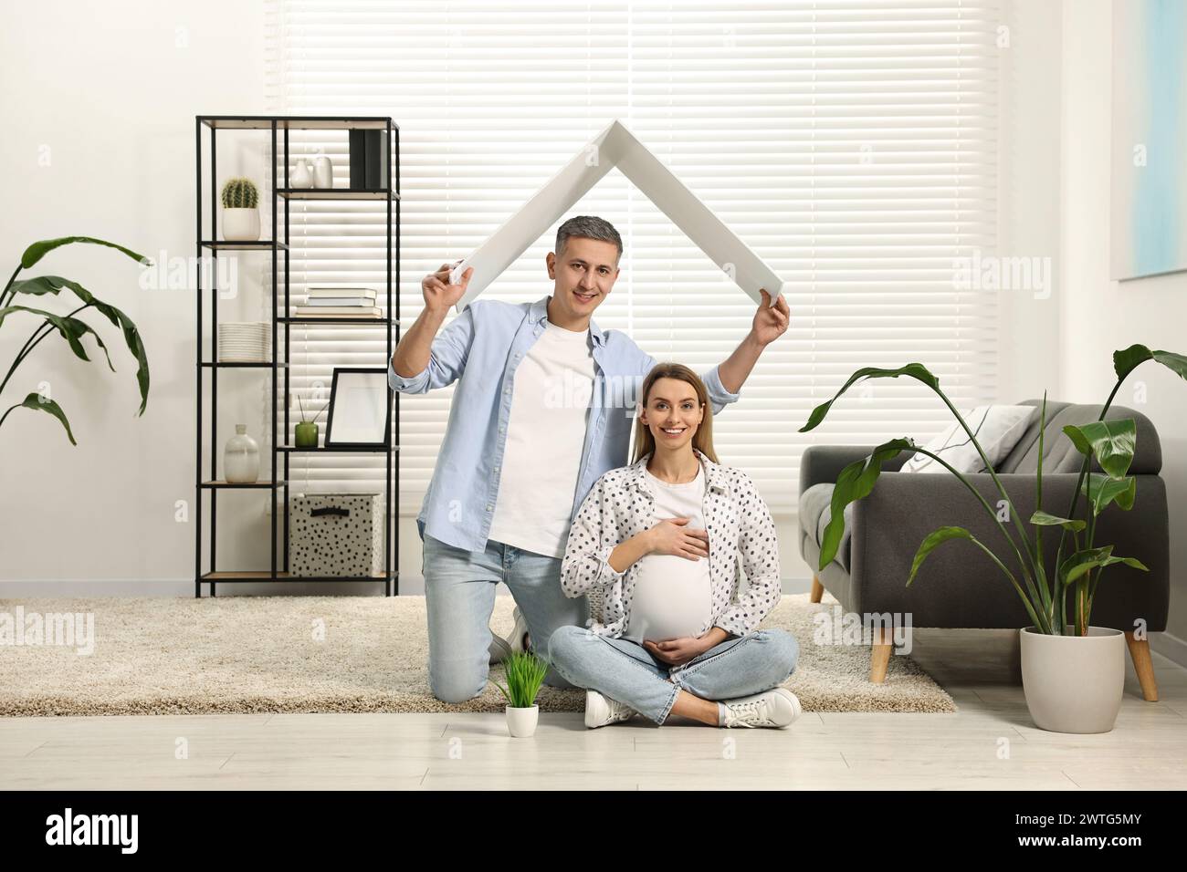 Concept de logement pour jeunes familles. Homme tenant un toit en carton au-dessus de sa femme enceinte tête à la maison Banque D'Images