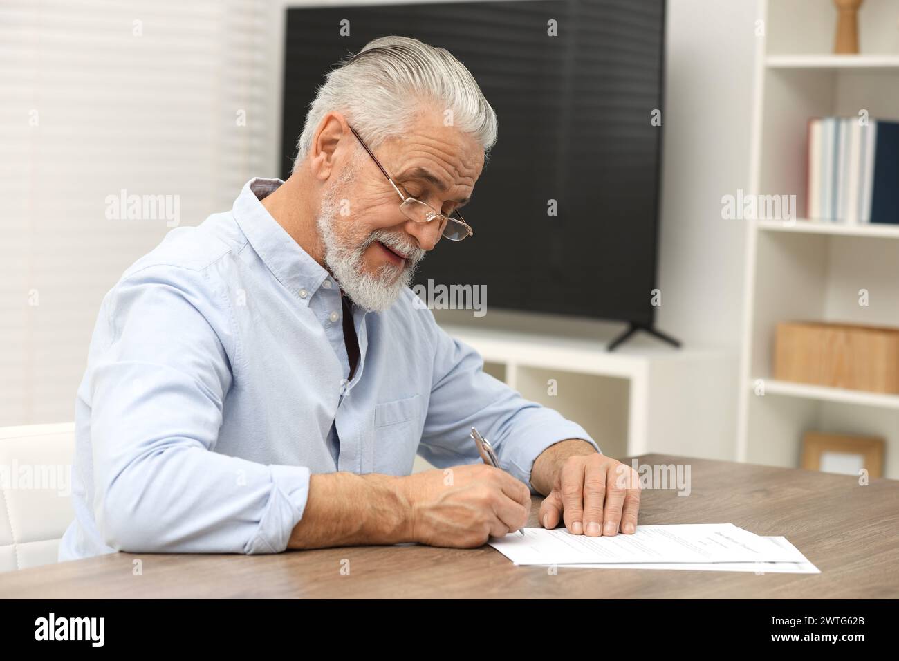 Homme senior signant dernier testament et testament à la table en bois à l'intérieur. Espace pour le texte Banque D'Images