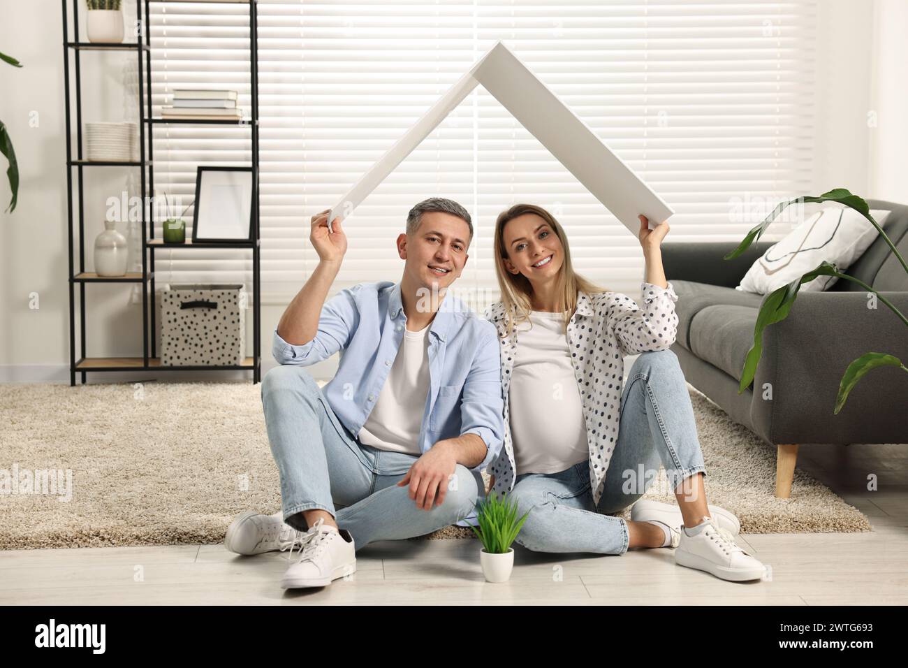 Concept de logement pour jeunes familles. Femme enceinte avec son mari assis sous un toit en carton sur le sol à la maison Banque D'Images