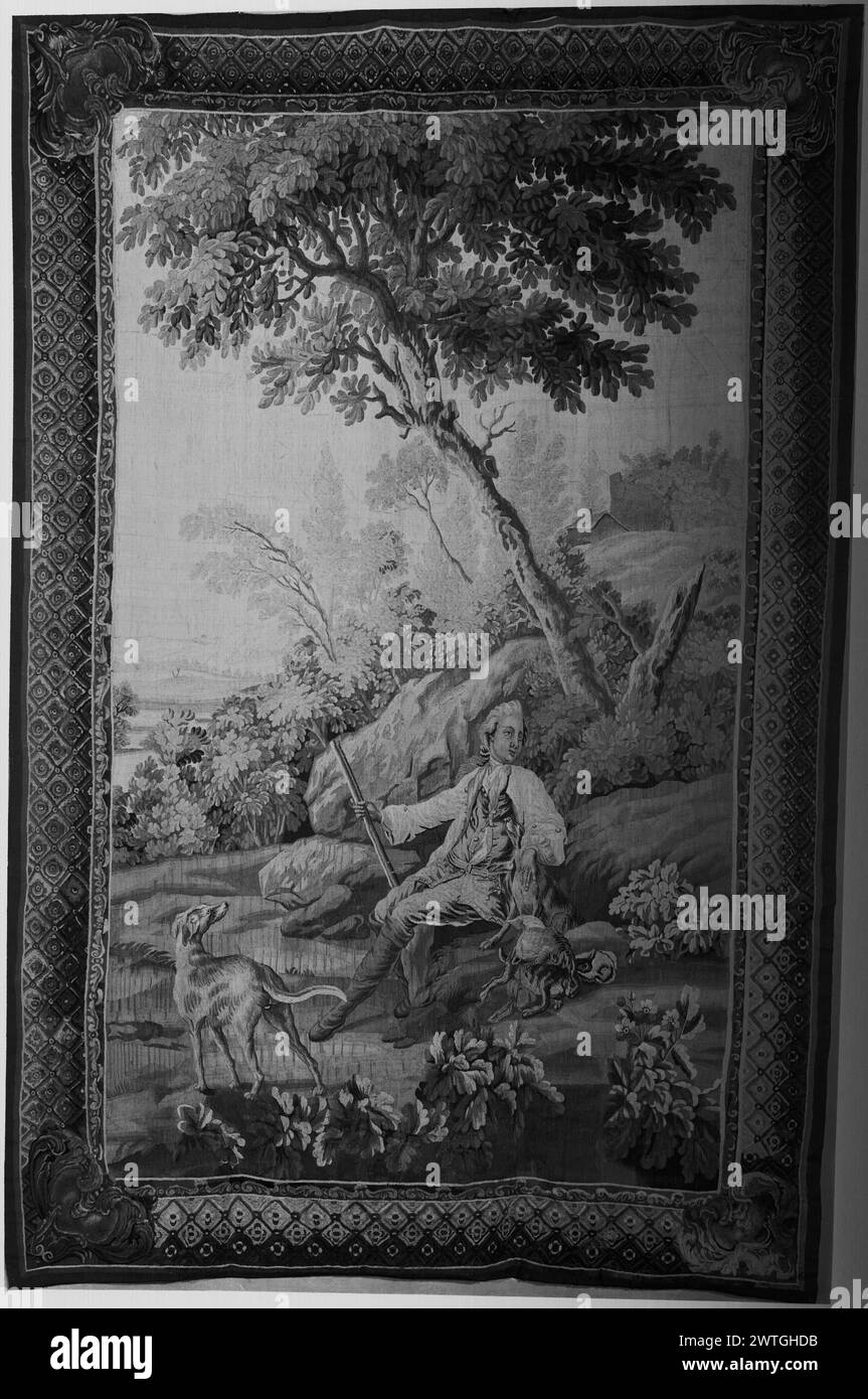 Chasseur se reposant avec des chiens. Inconnu c. 1750-1800 dimensions de tapisserie : H 8'10' x l 5'9' tapisserie matériaux/techniques : inconnu culture : Centre de tissage français : Aubusson historique de propriété : Français & Co. acheté de MRS H. S. Vanderbilt, facturé le 21/04/1942 ; vendu au Dr Nicolas Karger le 29/01/1959. Dans un paysage avec des arbres et des plantes à fleurs, un chasseur est assis sur un monticule herbeux tenant un morceau de volaille et tapotant un chien, à côté du gibier mort et avec un chien supplémentaire au premier plan; bâtiments sur le sommet de la colline dans la distance (R) (BRD) bordure de cadre d'image avec motif de treillis enfermant des rosettes, et feuilles d'acanthus défilées i Banque D'Images