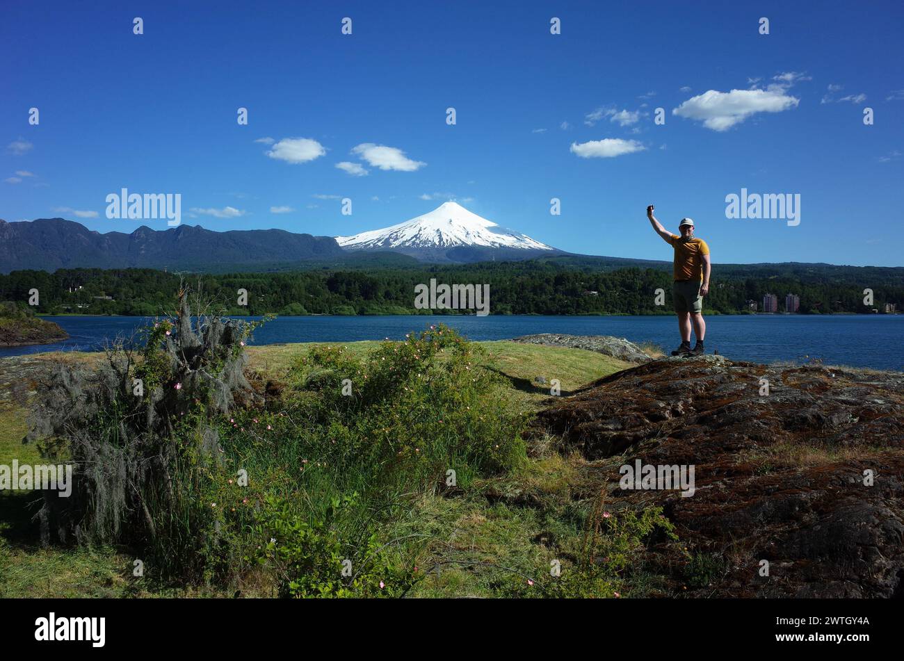 Homme touriste debout avec la main vers le haut posant pour la photo avec vue sur le volcan Villarrica enneigé et le lac Villarrica. Nature du Chili. Tourisme à Pucon Banque D'Images