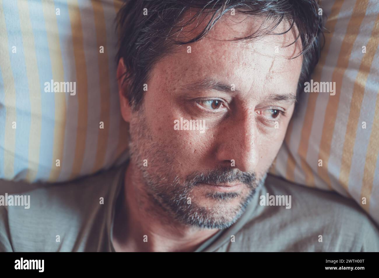 Homme déprimé allongé dans le lit sur un oreiller et regardant par la fenêtre, vue de dessus Banque D'Images