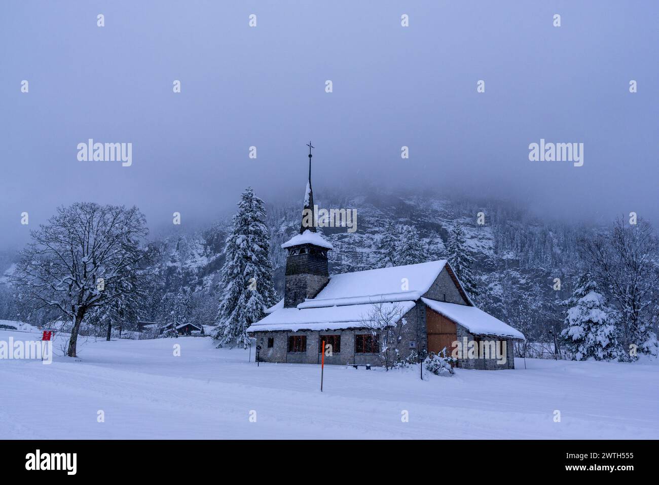Église Marienkirche dans les nuages bas et début de soirée chute de neige contre le bois de Holzfad, Kandersteg, Oberland bernois, Suisse Banque D'Images