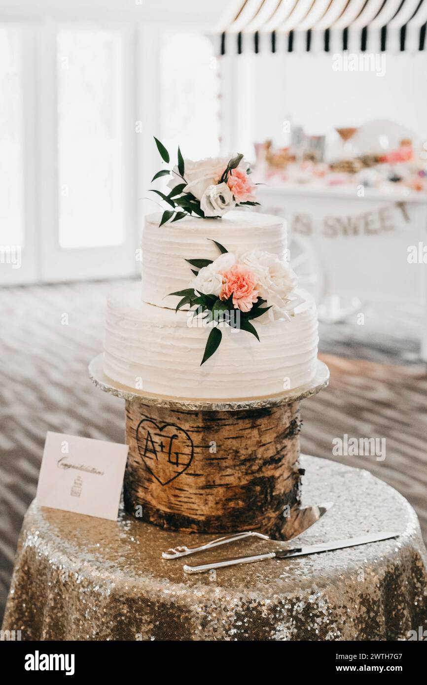 gâteau de mariage blanc avec de grandes fleurs sur le stand rustique Banque D'Images