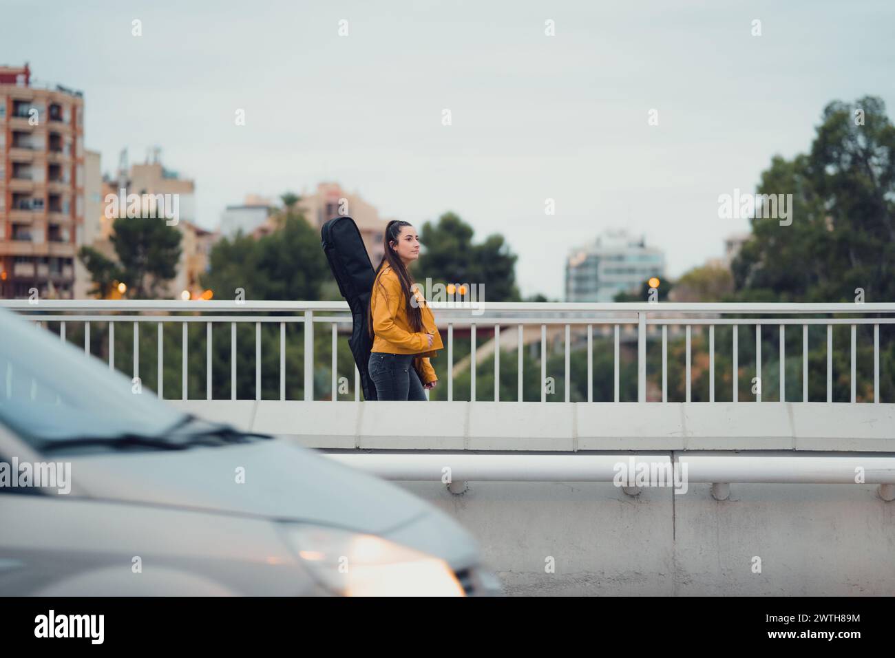 Jeune femme portant de la guitare sur son dos marchant à travers un pont urbain Banque D'Images
