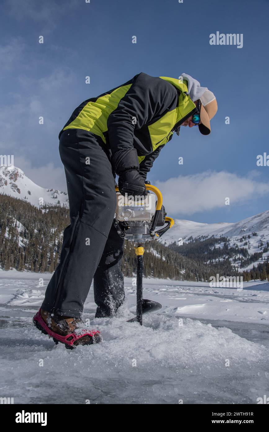 L'homme perce un trou de pêche de glace dans les montagnes du Colorado Banque D'Images