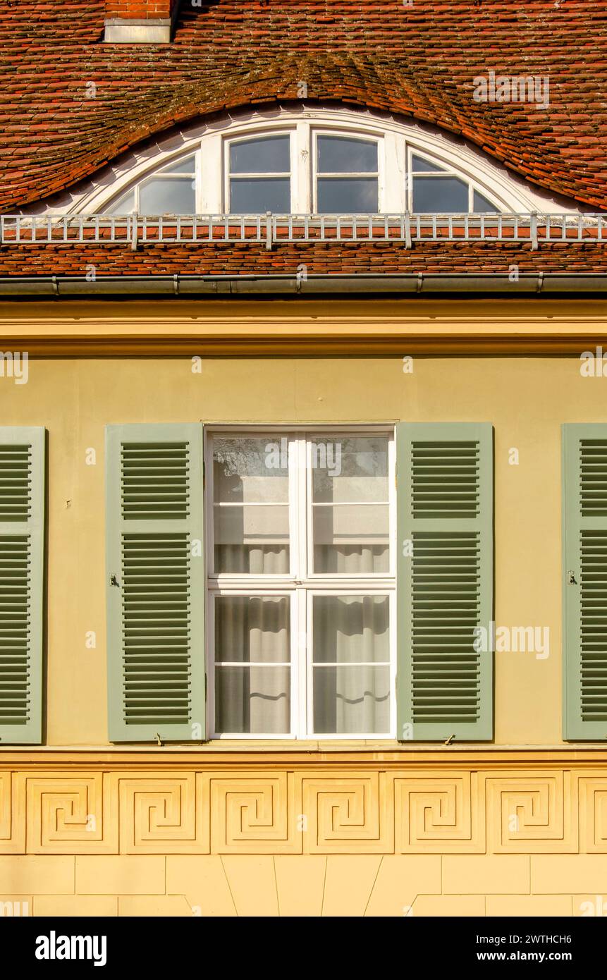 Potsdam, Allemagne, 9 mars 2024 : façade traditionnelle avec plâtre jaune, ardoise rouge, cadres de fenêtres blancs et volets verts Banque D'Images