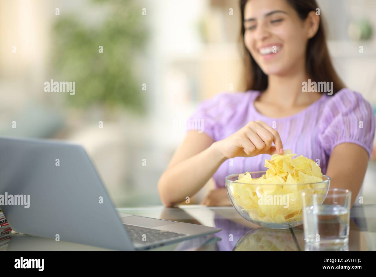 Femme heureuse regardant le film sur ordinateur portable manger des chips de pomme de terre à la maison Banque D'Images