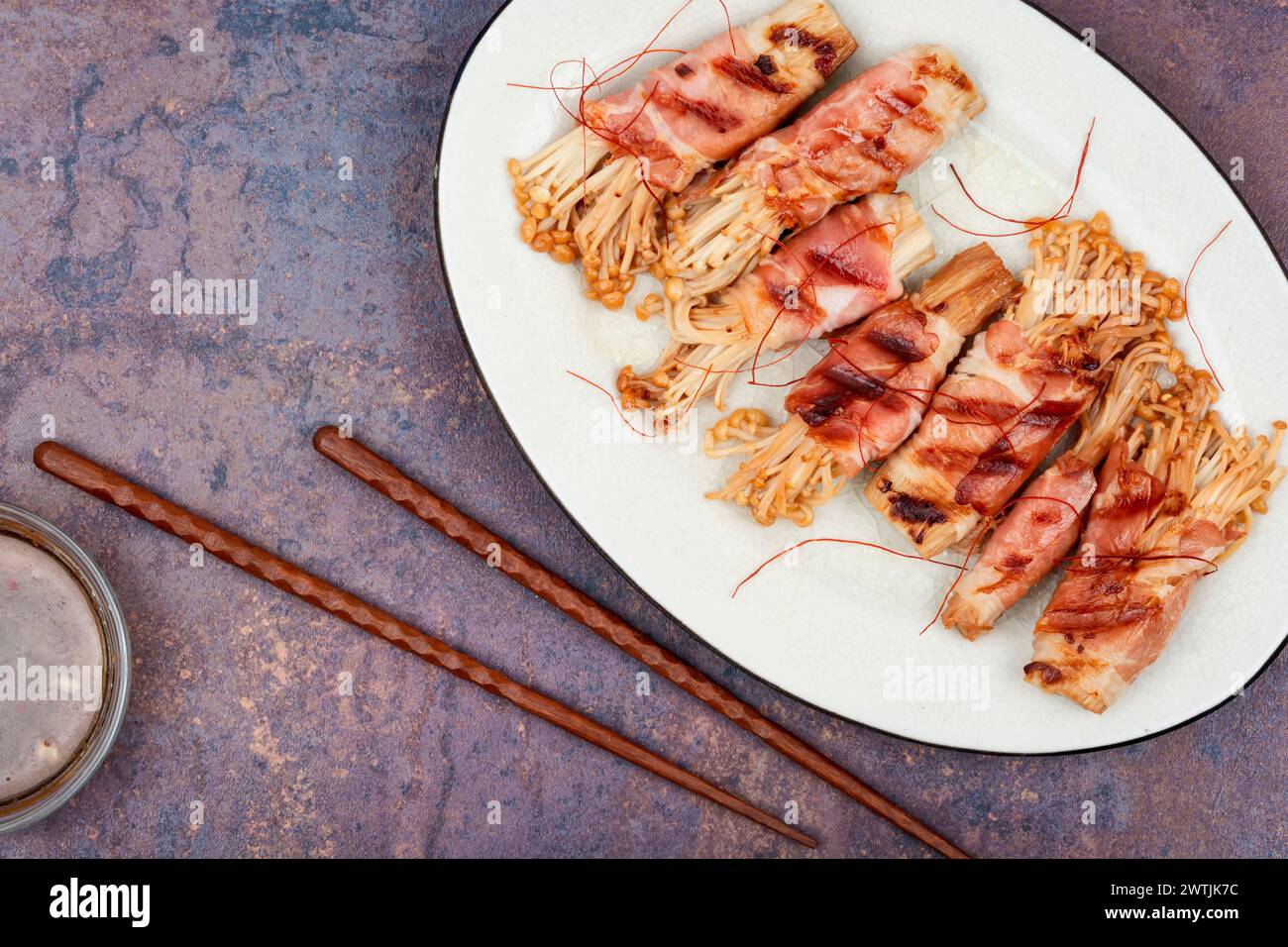 Champignon Enoki ou enokitake rôti au bacon sur assiette. Champignon enveloppé de bacon. Pose à plat avec espace de copie. Banque D'Images