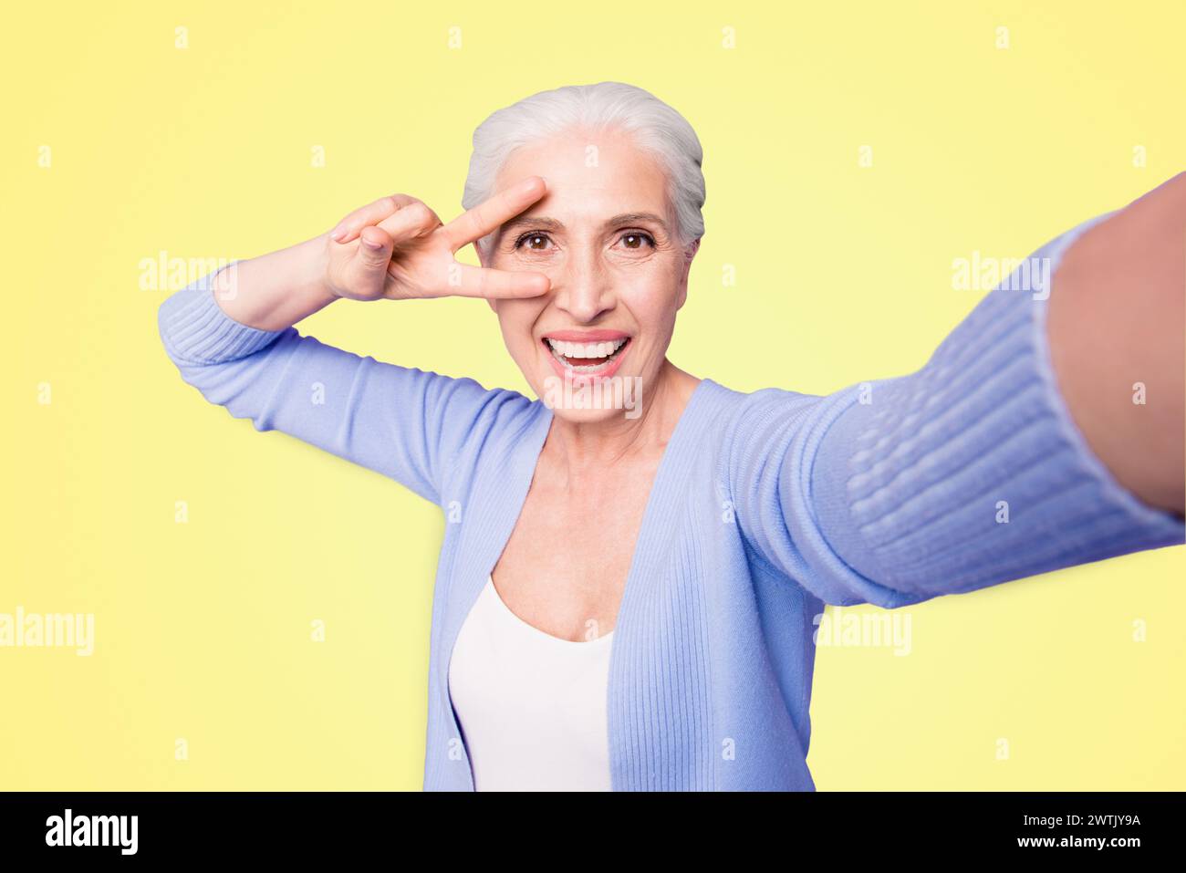 Une dame âgée fait un selfie sur l'appareil photo d'un smartphone faisant un v-sign près des yeux isolés sur fond violet clair avec un espace de copie pour le texte Banque D'Images