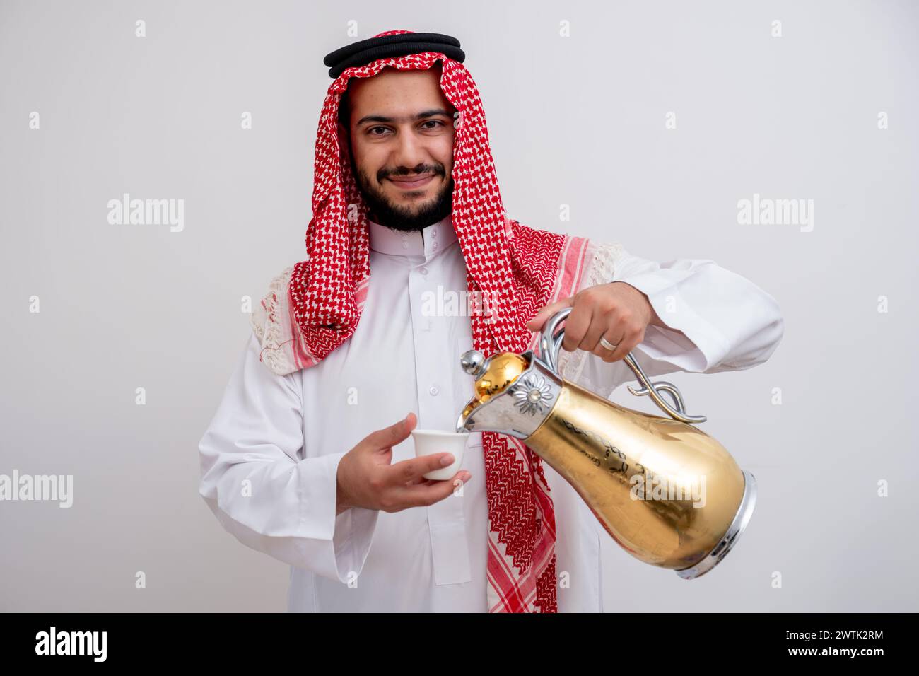 Homme arabe tenant une cafetière arabe portant de la dishdasha et de la kandura sur fond blanc isolé avec générosité et sentiments d'hospitalité Banque D'Images