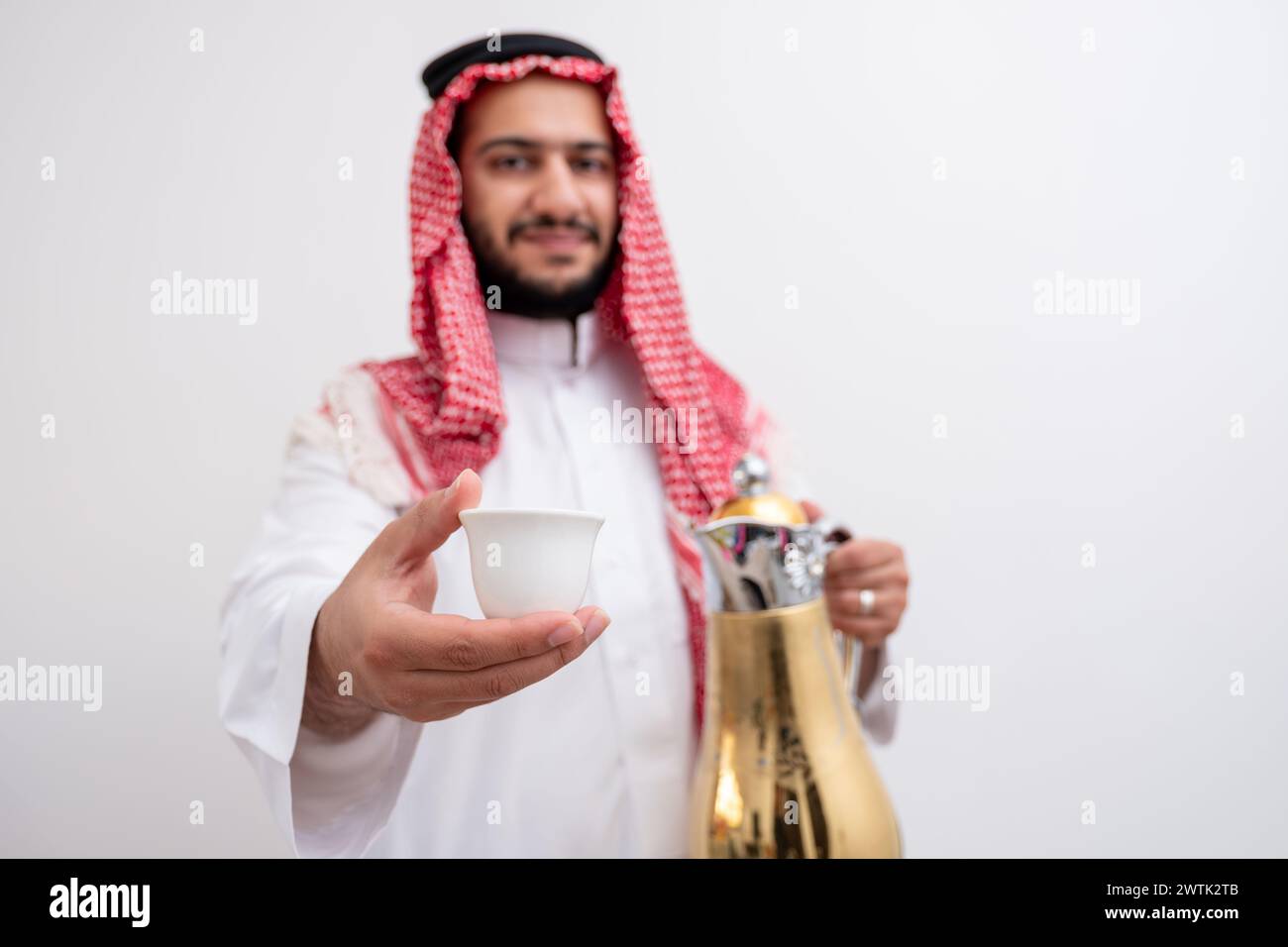 Homme arabe tenant une cafetière arabe portant de la dishdasha et de la kandura sur fond blanc isolé avec générosité et sentiments d'hospitalité Banque D'Images