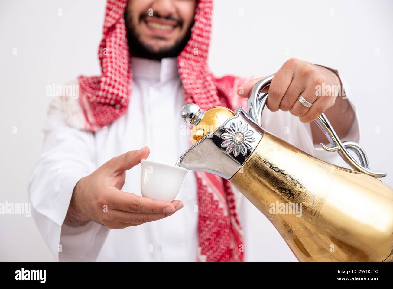Homme arabe tenant une cafetière arabe portant de la dishdasha et de la kandura sur fond blanc isolé avec générosité et sentiments d'hospitalité Banque D'Images