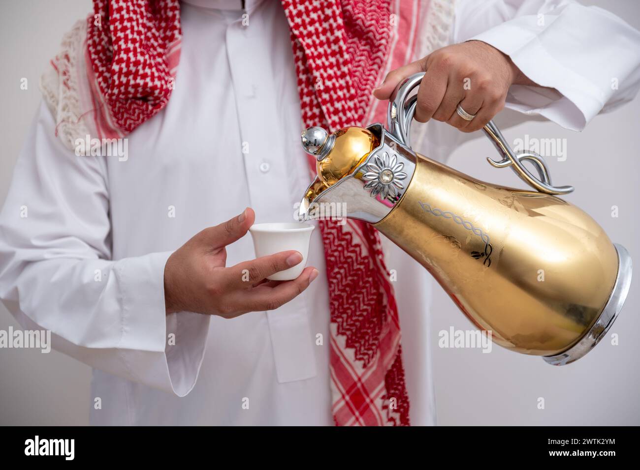 Homme arabe tenant une cafetière arabe portant de la dishdasha et de la kandura sur fond blanc isolé avec générosité et sentiments d'hospitalité Banque D'Images