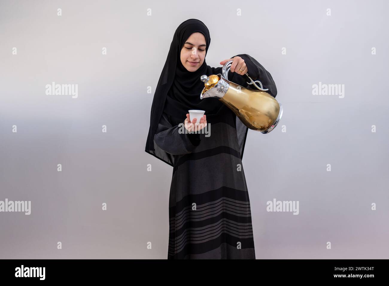 Exsudant la chaleur et la tradition, une femme arabe présente élégamment la tasse et la cafetière arabe chérie, un symbole d'hospitalité et de joie pendant Rama Banque D'Images