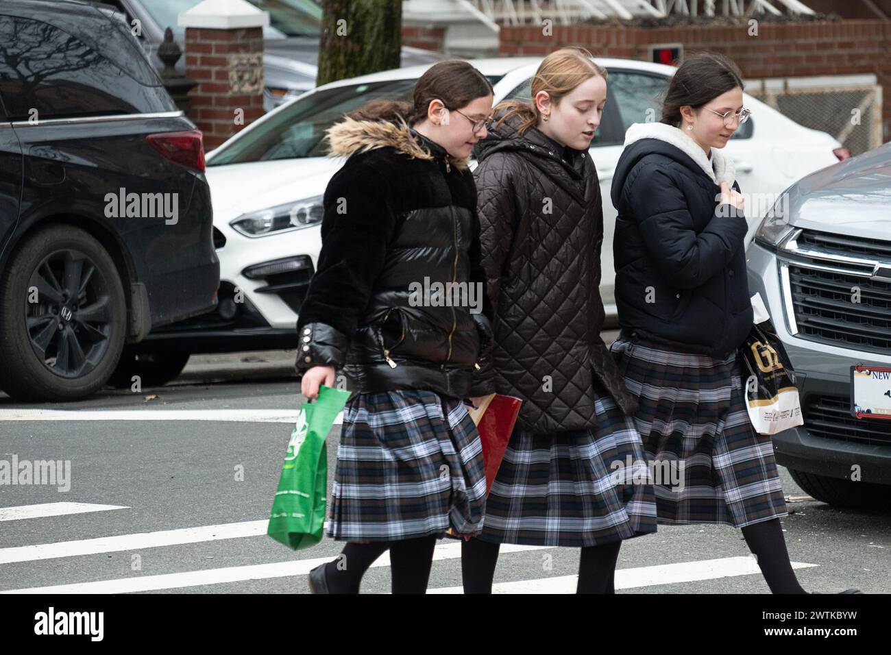 Des camarades de classe juifs orthodoxes portant les mêmes jupes tartan traversent une rue à Brooklyn, New York. Banque D'Images