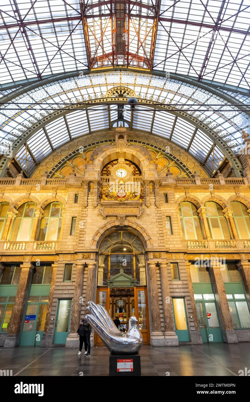 Anvers, Belgique, le 25 janvier 2024, cette image illustre la fusion splendide de l’art et du patrimoine architectural dans l’atrium de la gare centrale d’Anvers. Une sculpture moderne en argent se dresse au premier plan, attirant l'attention au milieu de la pierre classique et de l'horloge ornée de la gare sous le plafond complexe de fer et de verre. La présence de spectateurs ajoute de l'ampleur et de l'intérêt humain au cadre historique. Art et architecture à l'atrium de la gare centrale d'Anvers. Photo de haute qualité Banque D'Images