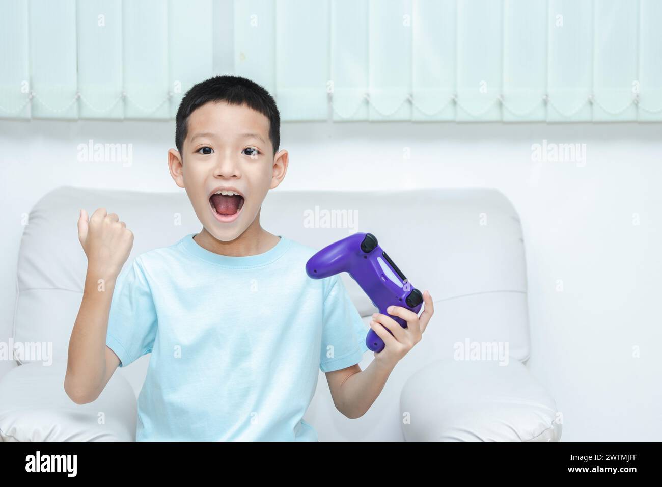 Petit garçon asiatique jouant à un jeu vidéo. plan d'un enfant tenant une manette de jeu. Asian Boy est ravi parce qu'il a gagné et lève les mains joyeusement. Banque D'Images