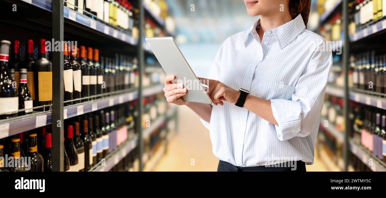 Femme responsable des ventes au détail analysant la performance commerciale du département d'alcool dans le supermarché. Employé féminin utilisant une tablette numérique dans un magasin d'alcool Banque D'Images