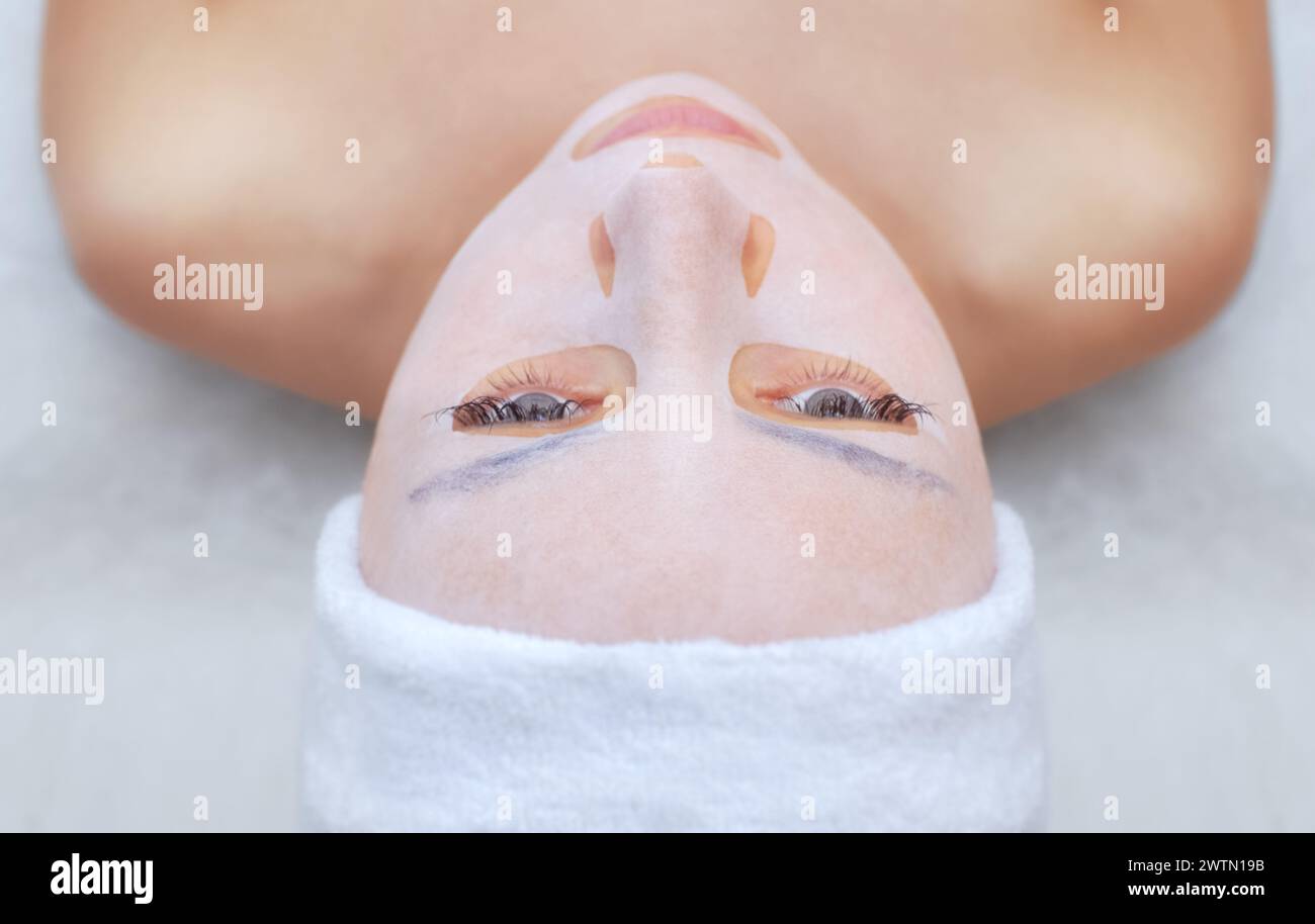 Le cosmétologue pour la procédure de nettoyage et d'hydratation de la peau, en appliquant un masque de feuille sur le visage d'une jeune femme dans le salon de beauté.cosmétologie Banque D'Images