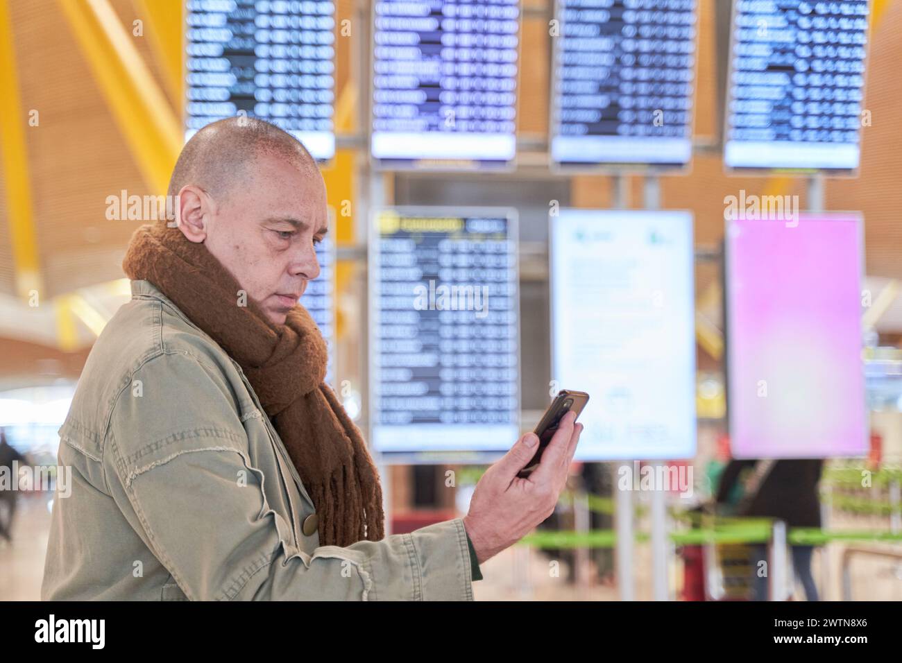 Vérification de l'état du vol : un homme jette un coup d'œil sur le téléphone et les informations de vol s'affichent en arrière-plan Banque D'Images