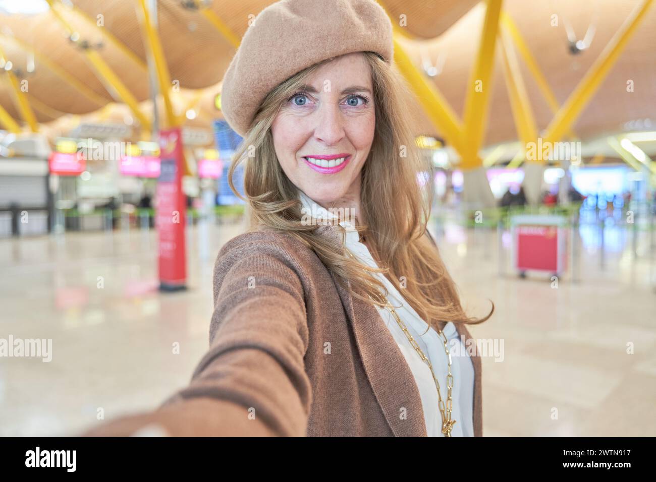femme blonde mature en vêtements d'automne et chapeau prenant un selfie dans le terminal de l'aéroport. photographiez avant de partir en voyage. copier l'espace pour le texte. Banque D'Images