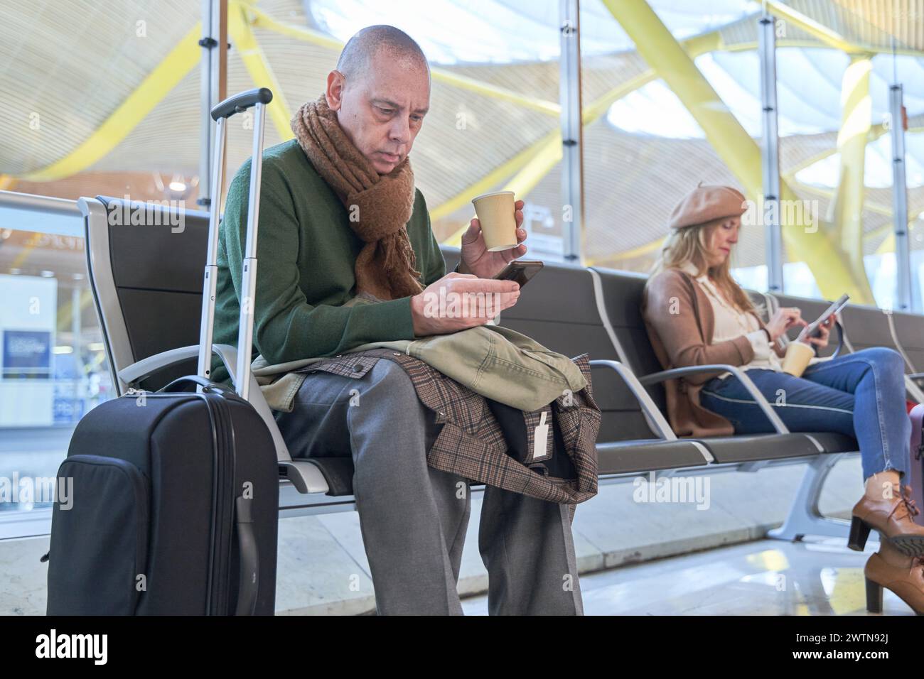 portrait d'un homme assis dans le salon de l'aéroport avec un café ou sa valise tout en utilisant son téléphone intelligent. Banque D'Images
