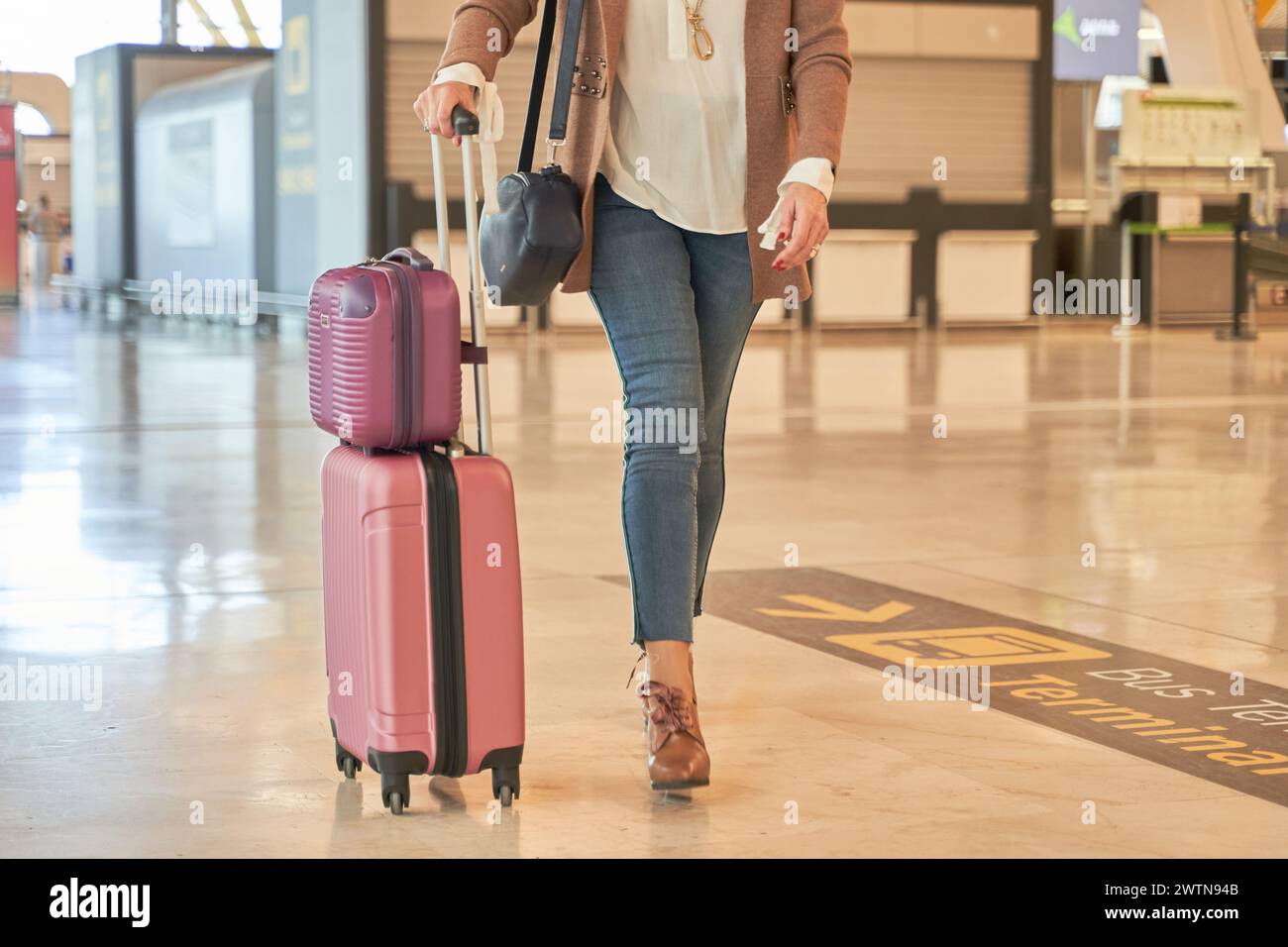 détail des jambes d'une femme marchant avec des valises de bagages à travers le terminal de l'aéroport. femme méconnaissable en vêtements décontractés Banque D'Images