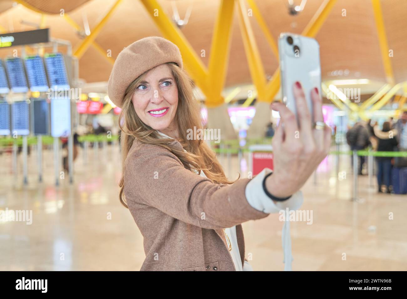 belle femme d'âge moyen prenant un selfie avec son téléphone intelligent à l'aéroport. portrait de femme élégante en chapeau Banque D'Images