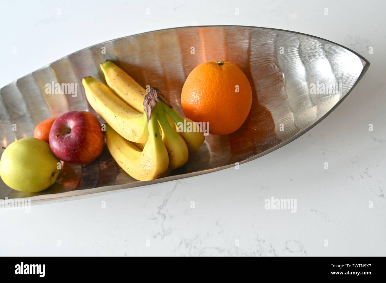 Variété de fruits dans un bol élégant sur un comptoir de cuisine blanc. Banque D'Images