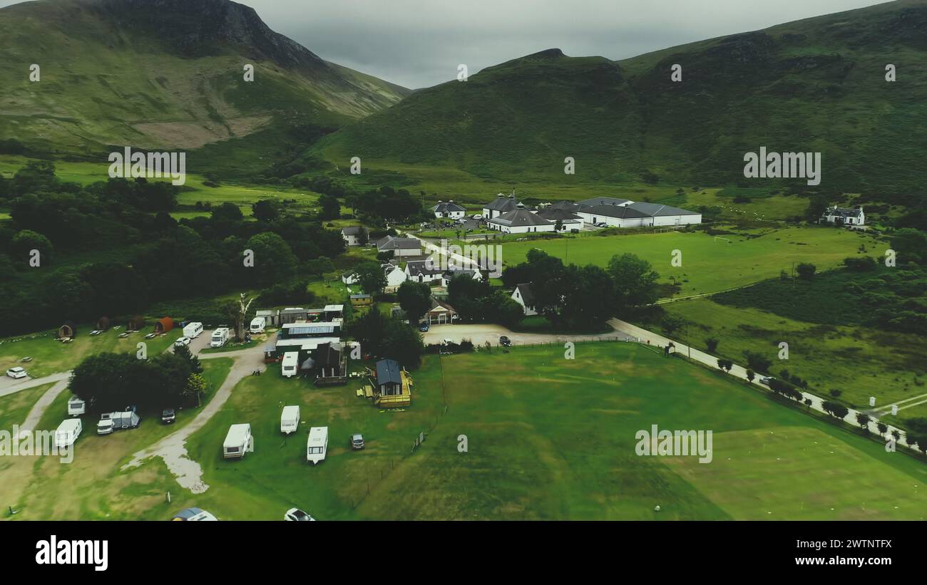 Vue aérienne du village écossais : route, chalets, maisons, distillerie, camping dans la vallée verte à la journée nuageuse d'été. Paysages de montagnes pittoresques de l'île d'Arran, en Écosse. Film filmé en cinéma Banque D'Images